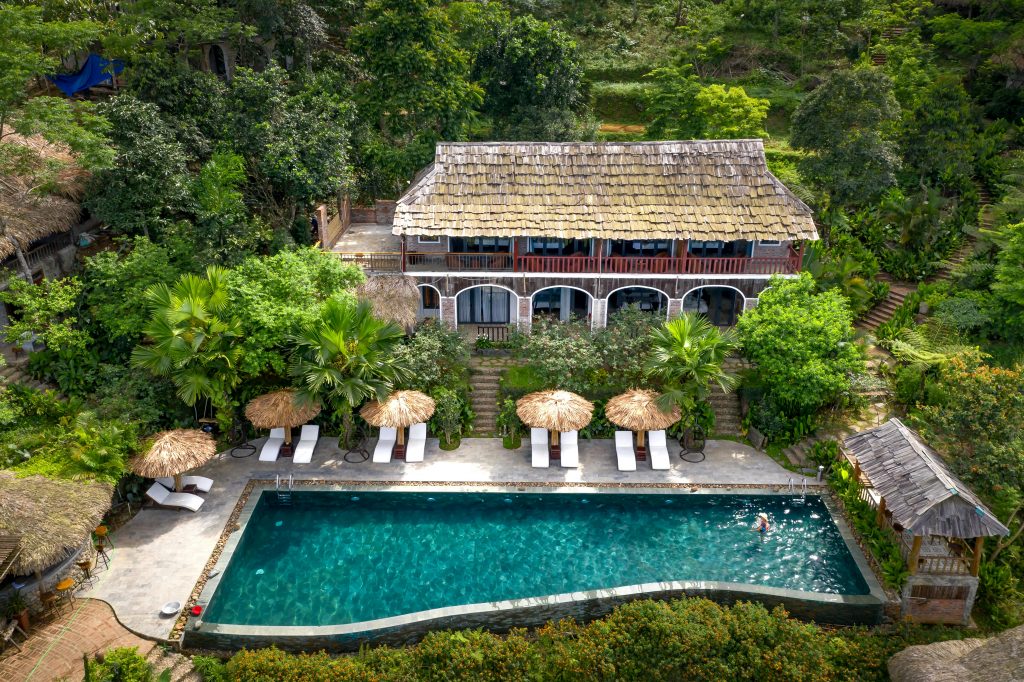 Aerial view of a luxurious tropical villa with a swimming pool surrounded by lush greenery.