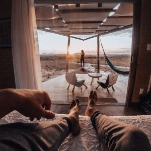 A cozy sunset view from bed, looking out to a patio with chairs and hammock in Brazil.