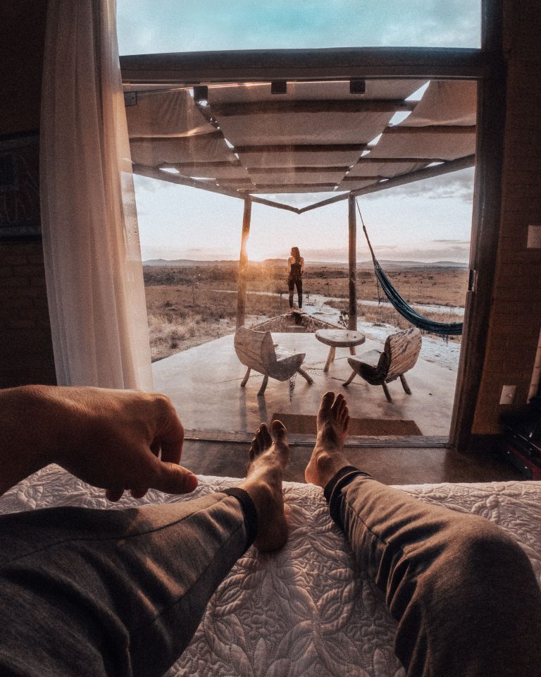 A cozy sunset view from bed, looking out to a patio with chairs and hammock in Brazil.