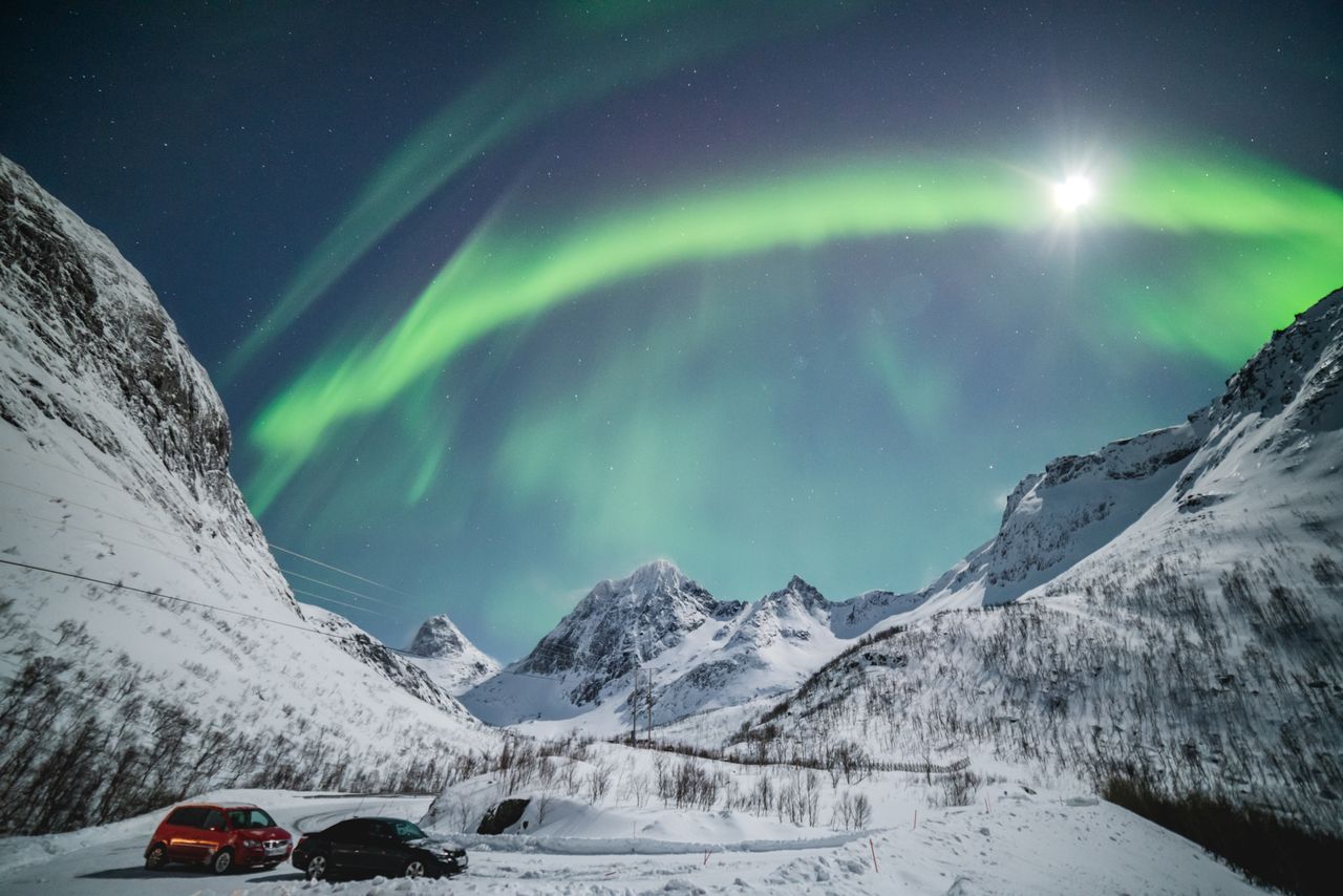 Aurora Borealis illuminates snowy peaks in Troms og Finnmark, Norway, under a starry sky.